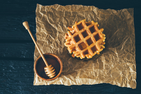 Belgian waffle and bowl of honey on dark wooden tableの写真素材