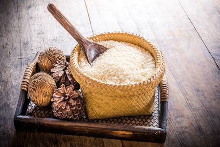 wooden spoon in basket of jasmine rice and pine cones on wooden tableの写真素材