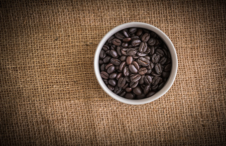 roasted coffee beans in white cup on sackcloth, can be used as a backgroundの写真素材