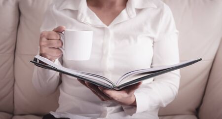woman is sitting on a sofa and reading a book while holding a coffee cup. retro style photoの写真素材
