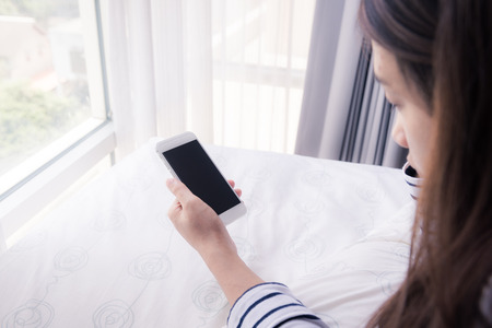 woman hands holding smartphone on bedの写真素材