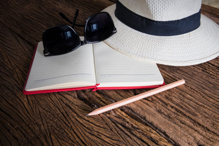 travel, summer vacation, tourism and objects concept. close up of hat, notebook, pencil and sunglasses on wooden table. Photo retro styleの写真素材