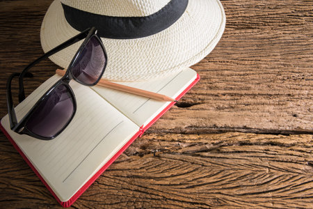 travel, summer vacation, tourism and objects concept. close up of hat, notebook, pencil and sunglasses on wooden table. Photo retro styleの写真素材