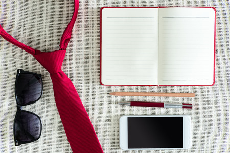 Open blank notebook, pen, pencil, smartphone, sunglasses on clean sackcloth with red necktie. Young business concept. Photo retro styleの写真素材