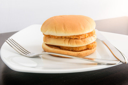 chicken hamburger in white plate  with knife and fork, on top wooden tableの写真素材