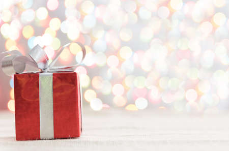 Decorative red gift box with a large silver bow and background bokeh of twinkling party lightsの写真素材