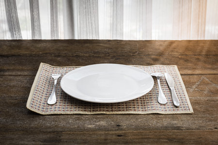 spoon, fork, knife and white dish on Platemat wooden background. Retro style Color