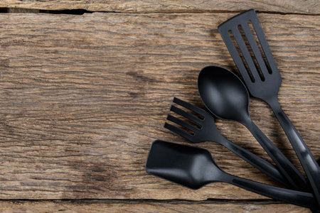 Top view of black plastic kitchen set skimmer, spade of frying pan on wooden background