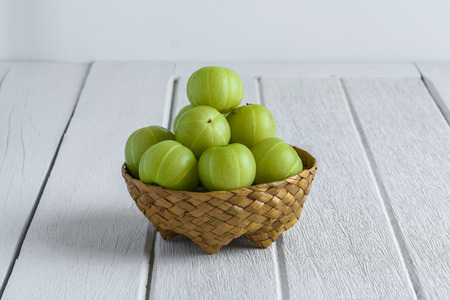 Indian gooseberry in Wicker basket on white wooden tableの写真素材