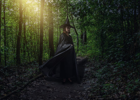 Portrait of woman in black Scary witch halloween costume with moonlight in a dark forest