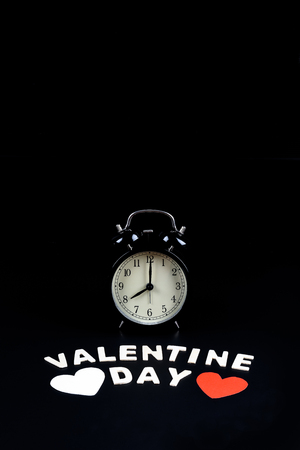 Alarm clock with heart shape and Wooden letters word "VALENTINE DAY" on black background. Concept of Valentine's dayの写真素材