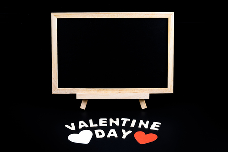 Empty Chalkboard on stand, Heart shape and Wooden letters word "VALENTINE DAY" on black background. Concept of Valentine's dayの写真素材
