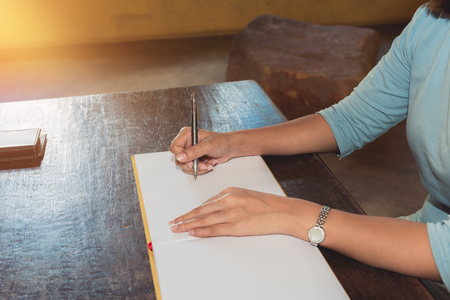 Womans hand signing a guest book with a pen and window light and shadowの写真素材