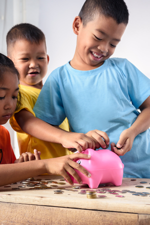 Group of asian children are helping putting coins into piggy bank on white background. Education Savings conceptsの写真素材