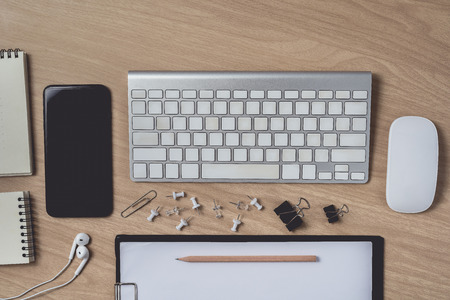 Workspace with diary or notebook and clipboard, mouse computer, keyboard, smart phone, Earphone, pencil, pen on wooden background. Flat lay, top view office table desk and copyspaceの写真素材