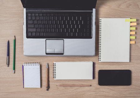 Workspace with diary or notebook and clipboard, laptop, mouse computer, keyboard, pencil, pen, sticky notes, smart phone on wooden background. Flat lay, top view office table desk and copyspaceの写真素材