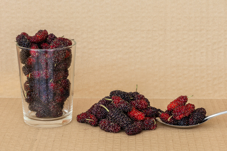 Organic Mulberry fruits in Stainless steel spoon and many pile of Mulberry friut on brown cardboard backgroundの写真素材
