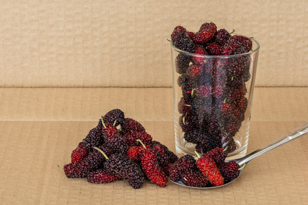 Organic Mulberry fruits in Stainless steel spoon and many pile of Mulberry friut on brown cardboard backgroundの写真素材