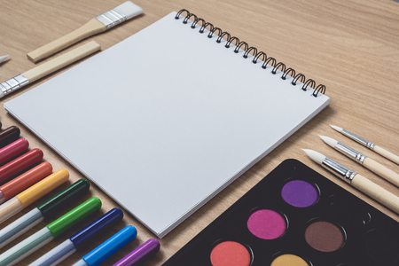 Notepad or notebook with Many colorful pens, paintbrush and Watercolor palette on brown wood table.using for Arts and Education background. Take note on book with paper and concept, copy space for your textの写真素材