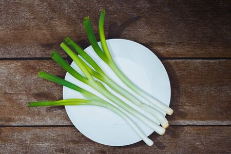 Japanese fresh green scallion or onion in white plate on wooden table background. Customize retro style imagesの写真素材