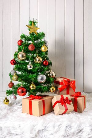 Christmas tree and ornaments with gifts boxes on white fur and white wooden backgroundの写真素材