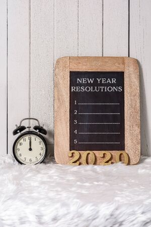 2020 wooden text and New Year's Resolutions List written on Notebook with Alarm clock on white fur and white wooden backgroundの写真素材