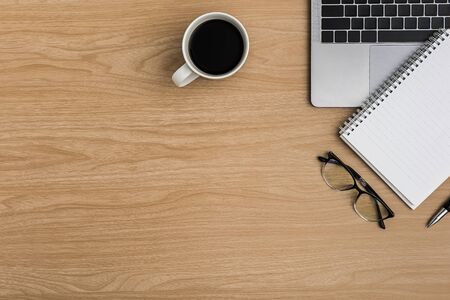 Top view Wood office desk table. Flat lay Workspace with eye glasses, laptop, notebook, pen, coffee cup office supplies on wooden backgroundの写真素材