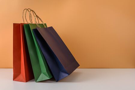 mockup of blank craft package or colorful paper shopping bag with handles on white table and pastel orange background. with copy space for your message and logoの写真素材
