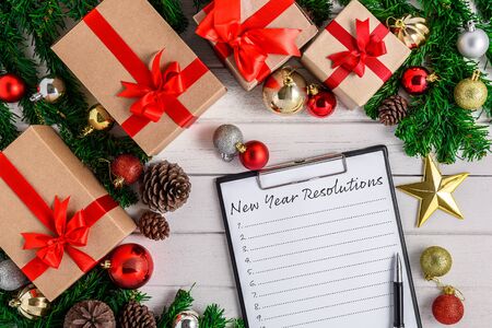 New Year's Resolutions List written on white paper on clipboard with Christmas fir tree and decoration on white wooden board. Top view with copy space. Christmas or New year backgroundの写真素材