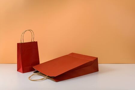 mockup of blank craft package or colorful paper shopping bag with handles on white table and pastel orange background. with copy space for your message and logoの写真素材
