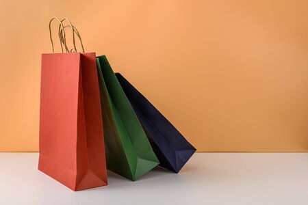 mockup of blank craft package or colorful paper shopping bag with handles on white table and pastel orange background. with copy space for your message and logoの写真素材