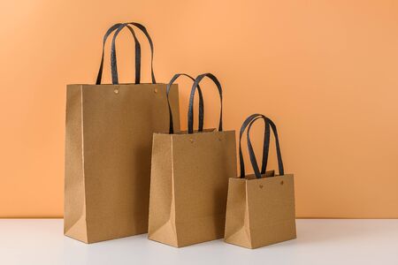 mockup of blank craft package or Brown paper shopping bag with handles on white table and pastel orange background. with copy space for your message and logoの写真素材