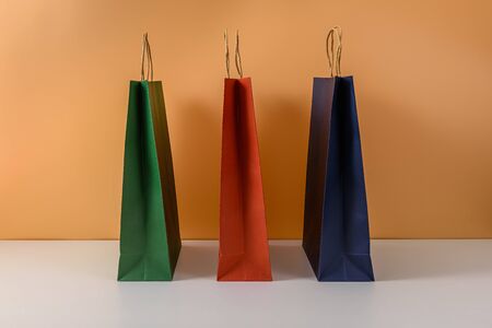 mockup of blank craft package or colorful paper shopping bag with handles on white table and pastel orange background. with copy space for your message and logoの写真素材