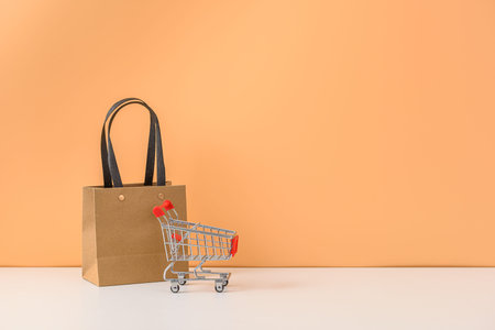 Paper shopping bags and shopping cart or trolley on white table and pastel orange background.の写真素材
