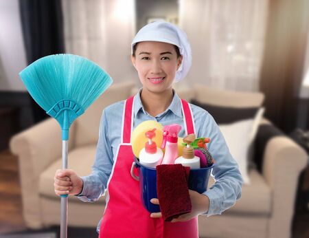 Cleaning concept Woman with bucket of washing fluids and rags in hands and cleaning equipment ready to clean house on blurred livingroom backgroundの写真素材