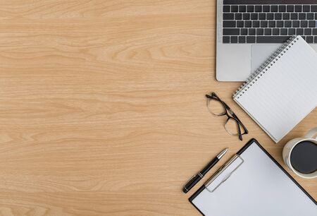 Top view Wood office desk table. Flat lay Workspace with eye glasses, laptop, notebook, clipboard, pen, coffee cup office supplies on wooden backgroundの写真素材