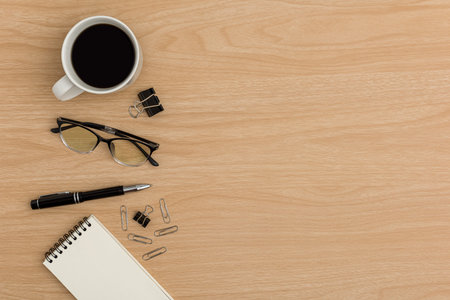 Top view office table desk. Flat lay Workspace with blank notebook, coffee cup, pen, paper clip, eye glasses office supplies on wooden table background.の写真素材