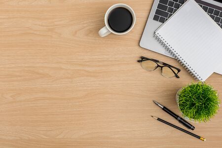 Top view Wood office desk table. Flat lay Workspace with eye glasses, laptop, tree pot, notebook, pen, pencil, coffee cup office supplies on wooden backgroundの写真素材