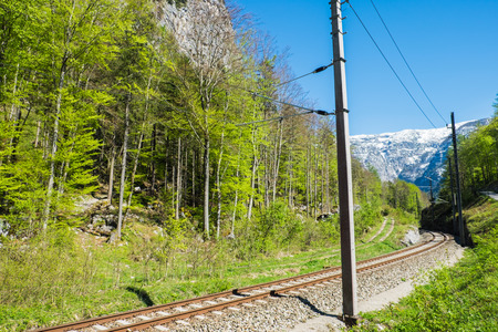 Railroad tracks to snow mountain have electric pole. The narrow-gauge railway along the ridge in clear blue sky day on summerの写真素材