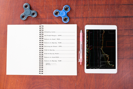 Stock graph on tablet, Pen, Black and blue hand spinner at the top blank notebook on wood table background,  The notebook had vocabulary about business and blank on  right side.の写真素材