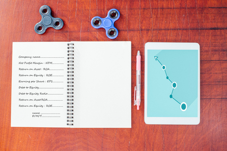 Blue graph on tablet, Pen, Black and blue hand spinner at the top notebook on wood table background, The notebook had vocabulary about business and blank on  left side.の写真素材