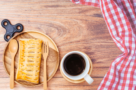 breakfast, Homemade pineapple pastries on vintage style wooden Plate set and cup of black coffee on wooden background, The napkin on right side and black spinner toy left side.の写真素材