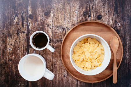 Top of view of cup of milk, black coffee  left side corn flakes, Dark wooden background, Right side had wheat cereal grain on wooden background.の写真素材