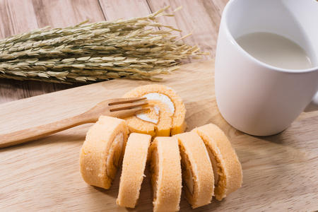 Breakfast set, Homemade orange swiss cake roll  and black coffee in white cup, Right side had wheat cereal grain on wooden background.の写真素材