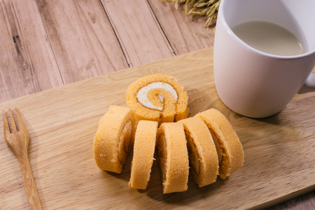 Breakfast set, Homemade orange swiss cake roll  and black coffee in white cup, Right side had wheat cereal grain on wooden background.の写真素材