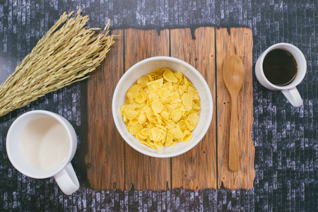Top of view of cup of milk, black coffee  left side corn flakes, Dark wooden background, Left side had wheat cereal grain on dark wooden background.の写真素材