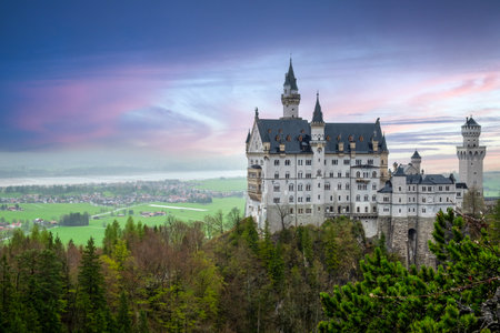 Neuschwanstein Castle at Sunset - A majestic view of the iconic Neuschwanstein Castle in Germany, perched on a rugged hill amidst lush green landscapes and a colorful sky. This fairy-tale castle, with its stunning architecture and picturesque surroundings, is a perfect representation of romantic historicism.の写真素材