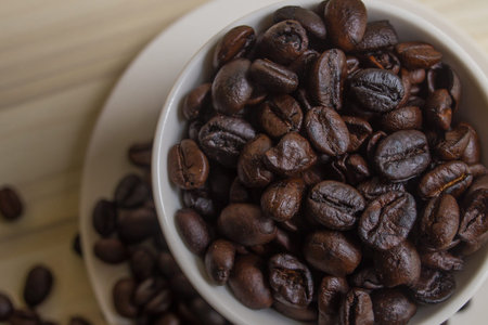 Roasted coffee beans in white cup on wood table