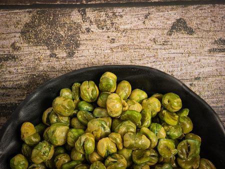 The salted green peas in black bowl on wood table.