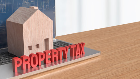 A wooden house model and bold  PROPERTY TAX text displayed on a laptop with architectural blueprints, representing real estate taxation, online assessment, financial planning, and property investment concepts.の写真素材